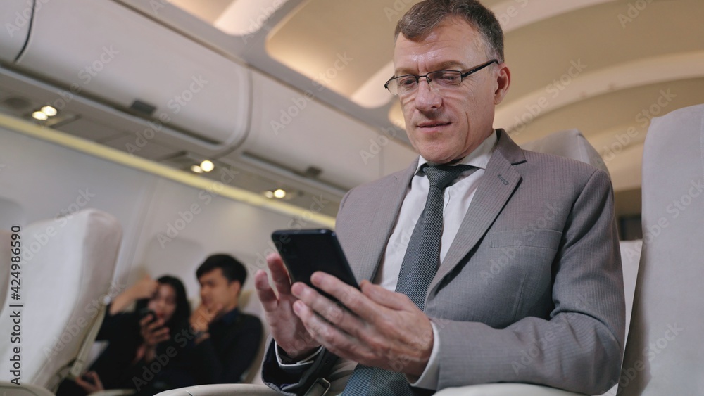Business man texting in smartphone in airplane. Caucasian businessman using smart phone in first class section of commercial airliner. Detail view of man's hand with camera dolly movement.