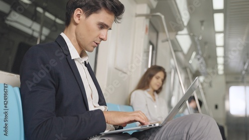 Businessman using laptop for working in the train and communicates on wireless headphones. Caucasian white male working on laptop while traveling by train.