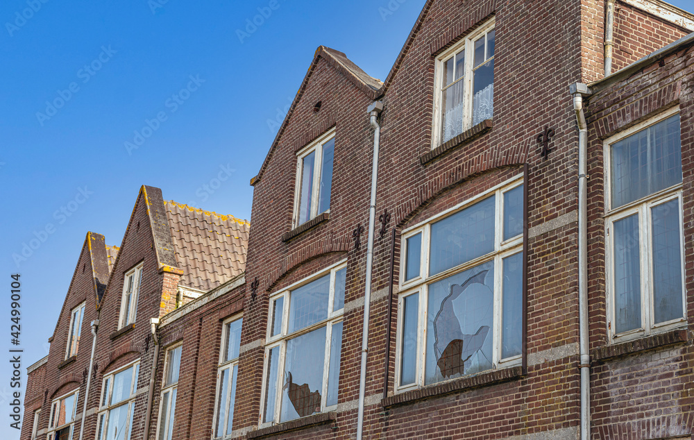 Old Dutch houses ready for demolition. Some windows are broken and mesh has been applied against squatters. The photo was taken on a sunny day with a clear blue sky in the beginning of spring.