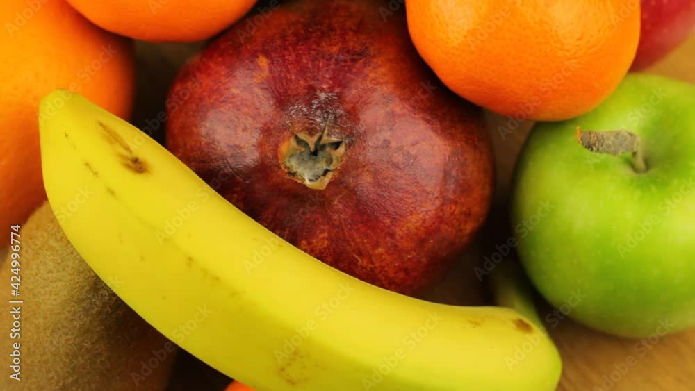 Rotating a heap of different fruits. Close-up video with banana, apples, tangerines, oranges, kiwi, pomegranate on a wooden board. Rotating a heap of different fruits. Close-up video with banana, apples, tangerines, oranges, kiwi, pomegranate on a wooden board.