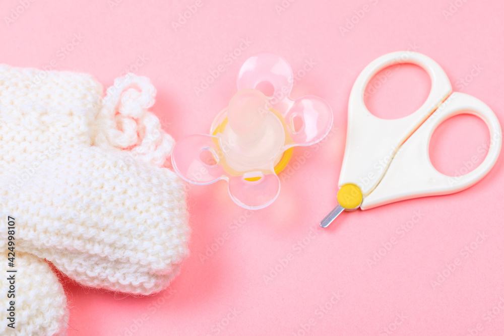 safe scissors, soother and booties for babies on pastel pink background .