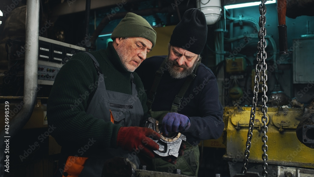 Male technicians examining engine parts together Male technicians examining engine parts together