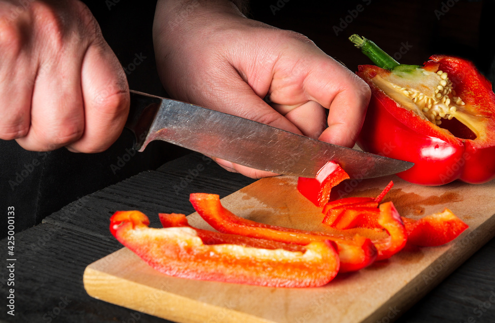 Close-up of a chef hands cutting peppers on cutting board. Professional preparation of salad in the kitchen in a restaurant or cafe. Side view