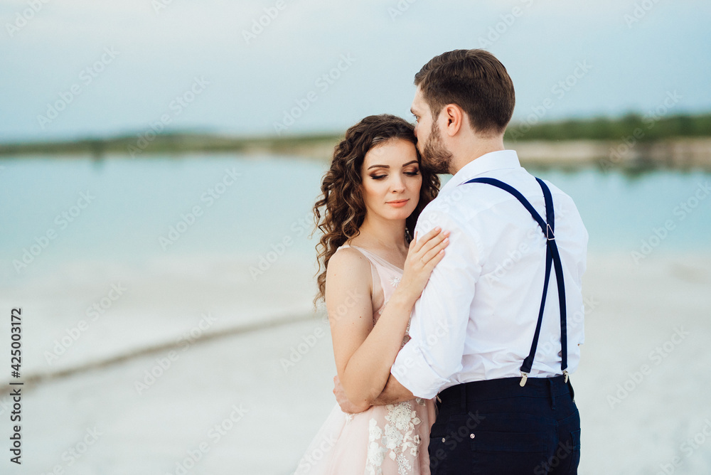 young couple a guy in black breeches and a girl in a pink dress are walking along the white sand young couple a guy in black breeches and a girl in a pink dress are walking along the white sand