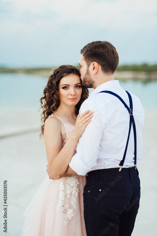 young couple a guy in black breeches and a girl in a pink dress are walking along the white sand