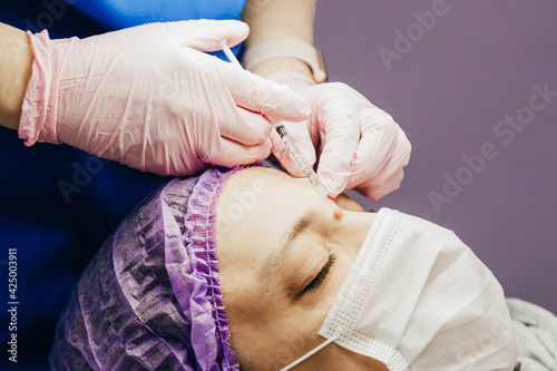 Surgeon in gloves gives injection of local anesthesia to patient before laser removing mole, closeup view.