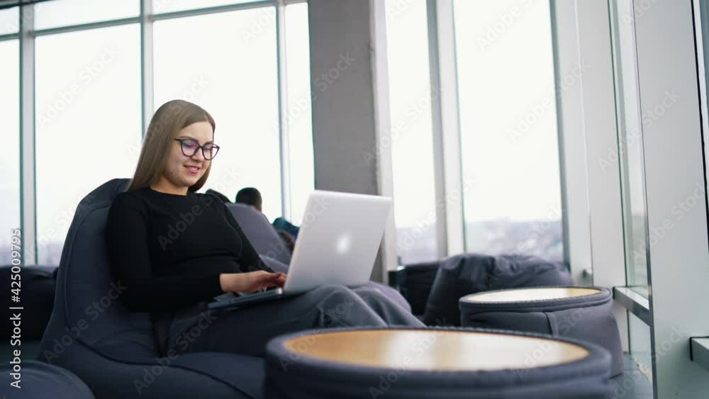 Young woman works on a laptop. Beautiful businesswoman in glasses sitting in a comfortable armchair using laptop in business centre. Young woman works on a laptop. Beautiful businesswoman in glasses sitting in a comfortable armchair using laptop in business centre.