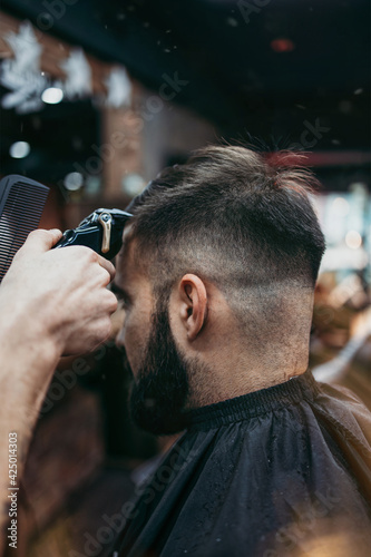 Good looking young adult man getting a hair and beard styling and dressing treatment by professional hairstylist.