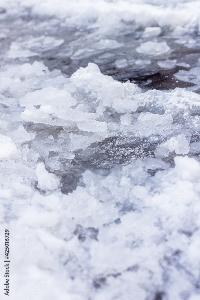 Close up photo of uneven ice. Blue, black, white frozen icy path covered with snow and black ice 