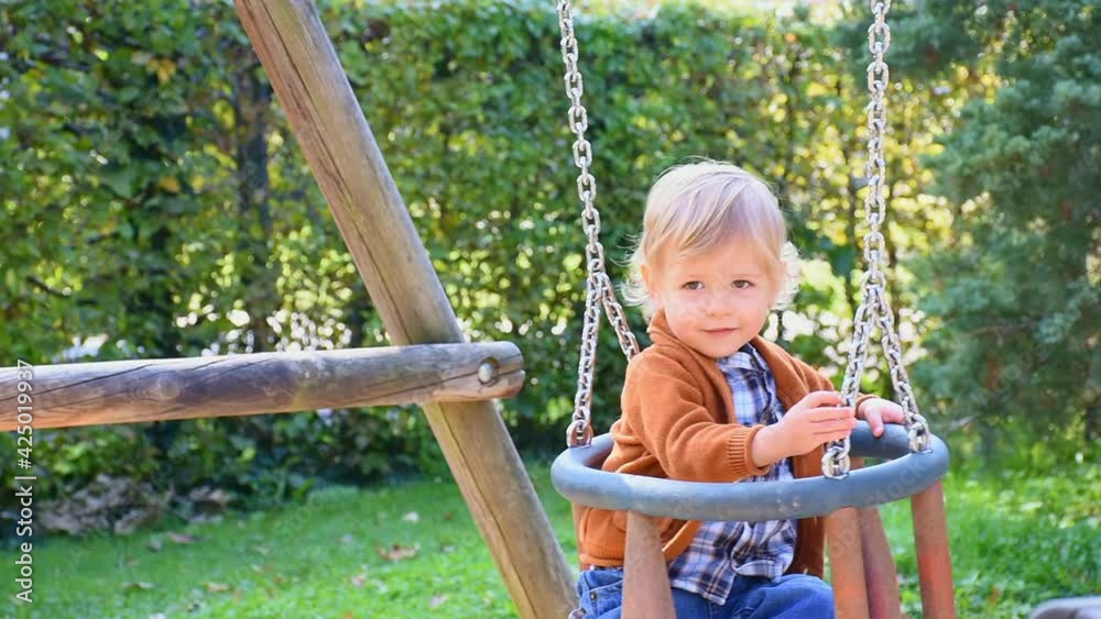 Happy cute little child having fun on a swing in the park, sunny warm autumn day in children playground Happy cute little child having fun on a swing in the park, sunny warm autumn day in children playground