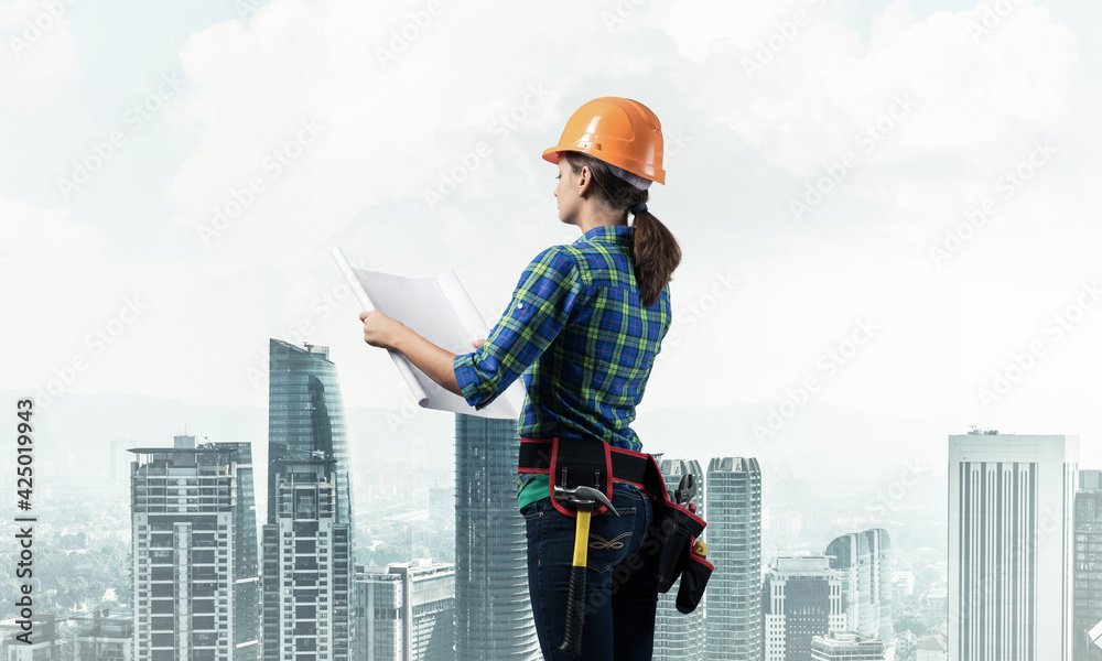Female engineer in hardhat standing with blueprint Female engineer in hardhat standing with blueprint