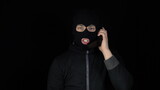 A man in a balaclava mask with a phone from the 90s. The bandit is talking on the phone. On a black background.