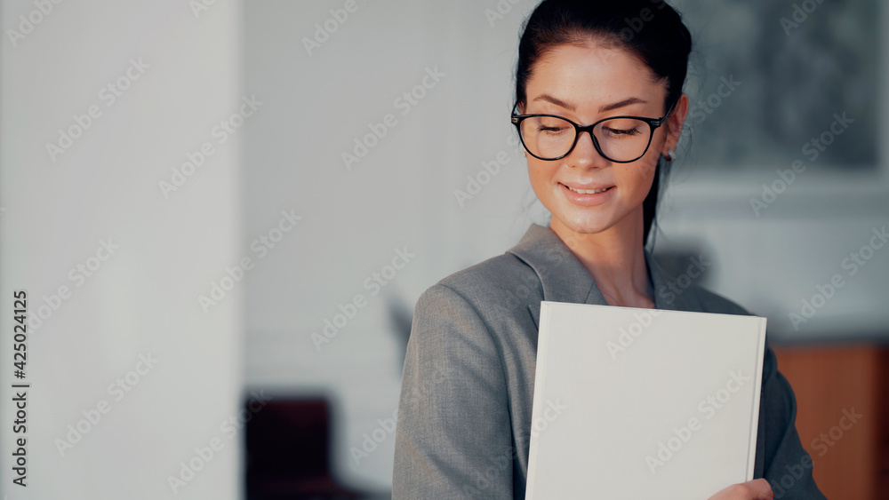 Holds the documents report book folder in his hands. Lawyer business woman in modern glasses in the office coworking. European-looking brunette in a gray suit. Copy space. Holds the documents report book folder in his hands. Lawyer business woman in modern glasses in the office coworking. European-looking brunette in a gray suit. Copy space.