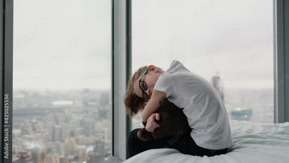 Cute teenage girl sits hugging her favorite toy on the bed near the window with a city view from above Cute teenage girl sits hugging her favorite toy on the bed near the window with a city view from above