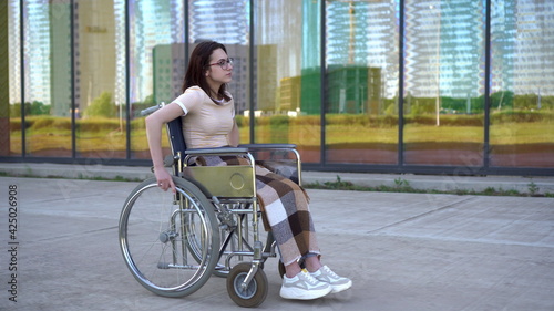 Young woman in a wheelchair. A girl rides in a wheelchair against the background of a glass building. Special transport for the disabled.