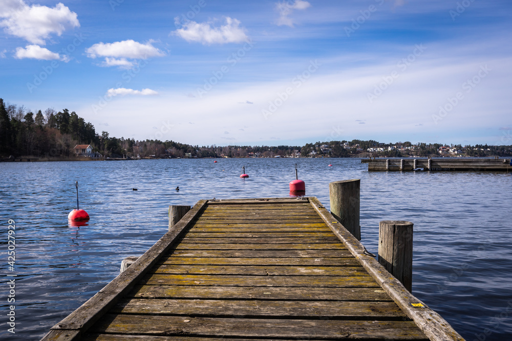 Obraz premium Old wooden pier or jetty for yachts and boats. Spring landscape of the coast of Sweden. Forest islands with evergreen trees in the gulf of the Baltic Sea. Panoramic view of Scandinavia in early spring
