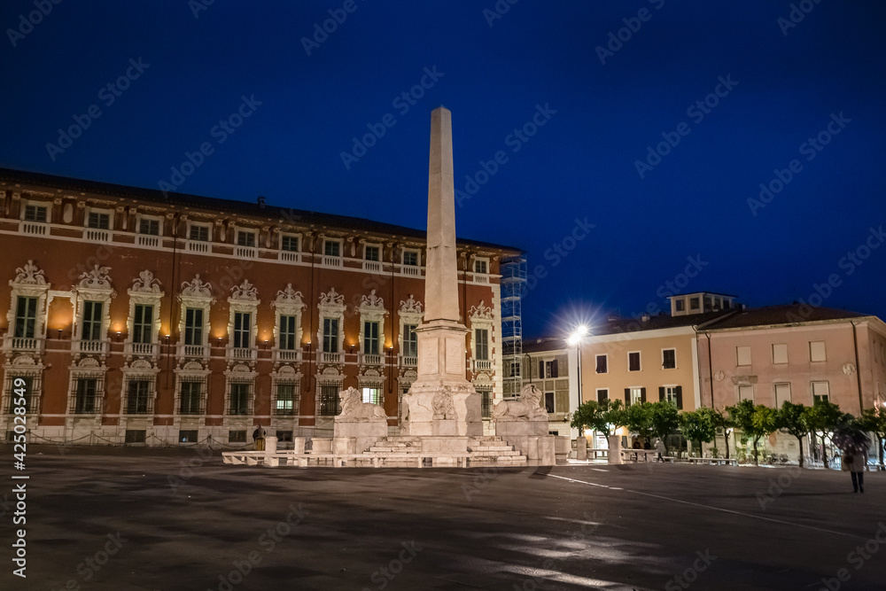 Cityscape. View of Piazza Aranci in Massa with the commemorative monument in the center and on the background the Ducal Palace at night illumination in Massa Tuscany Italy