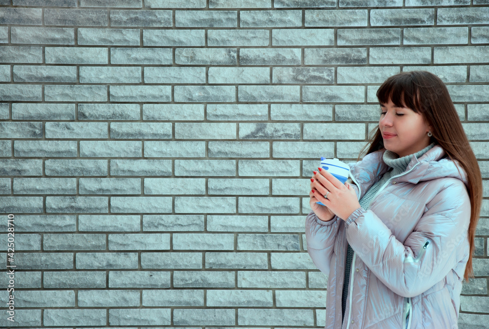 a young girl holds a silicone reusable coffee cup against a grey brick wall. High quality photo