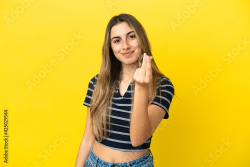 Young caucasian woman isolated on yellow background making money gesture