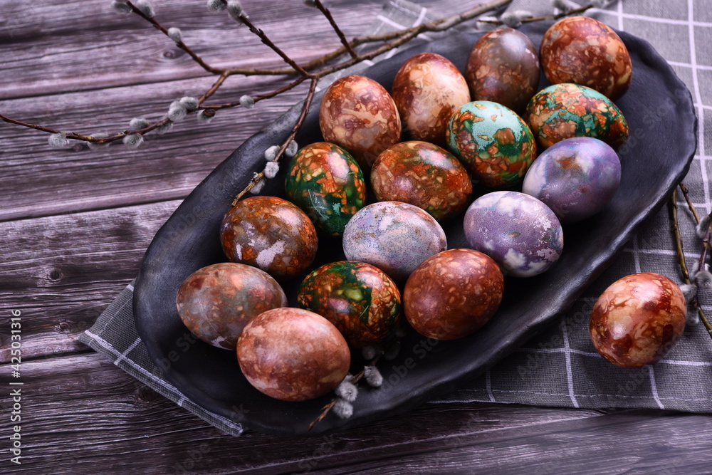 Obraz premium Naturally painted Easter eggs in a black clay plate on a rustic wooden background. Easter eggs painted with onion skins