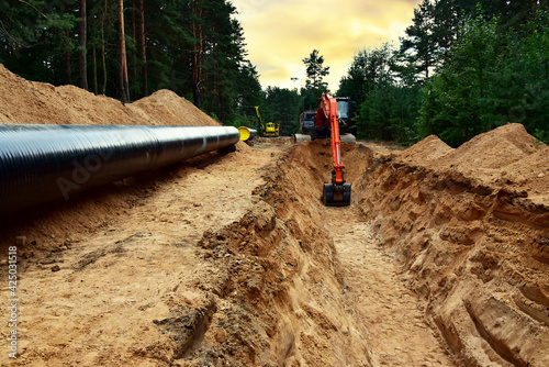 Excavator dig trench at forest area sunset background. Backgoe on earthwork for laying crude oil and natural gas pipeline or water main pipes. Natural gas pipeline construction
