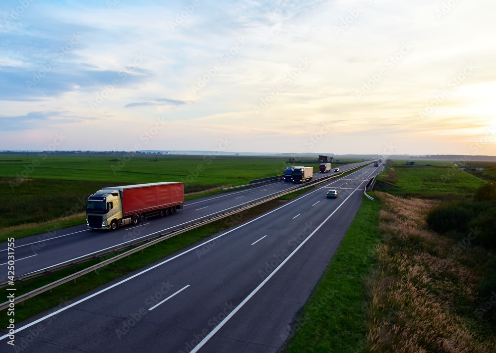 Truck with semi-trailer driving along highway on the sunset background. Goods delivery by roads. Services and Transport logistics. Modern Lorry and traаfic transport concept. Long Self-driving Truck with semi-trailer driving along highway on the sunset background. Goods delivery by roads. Services and Transport logistics. Modern Lorry and traаfic transport concept. Long Self-driving