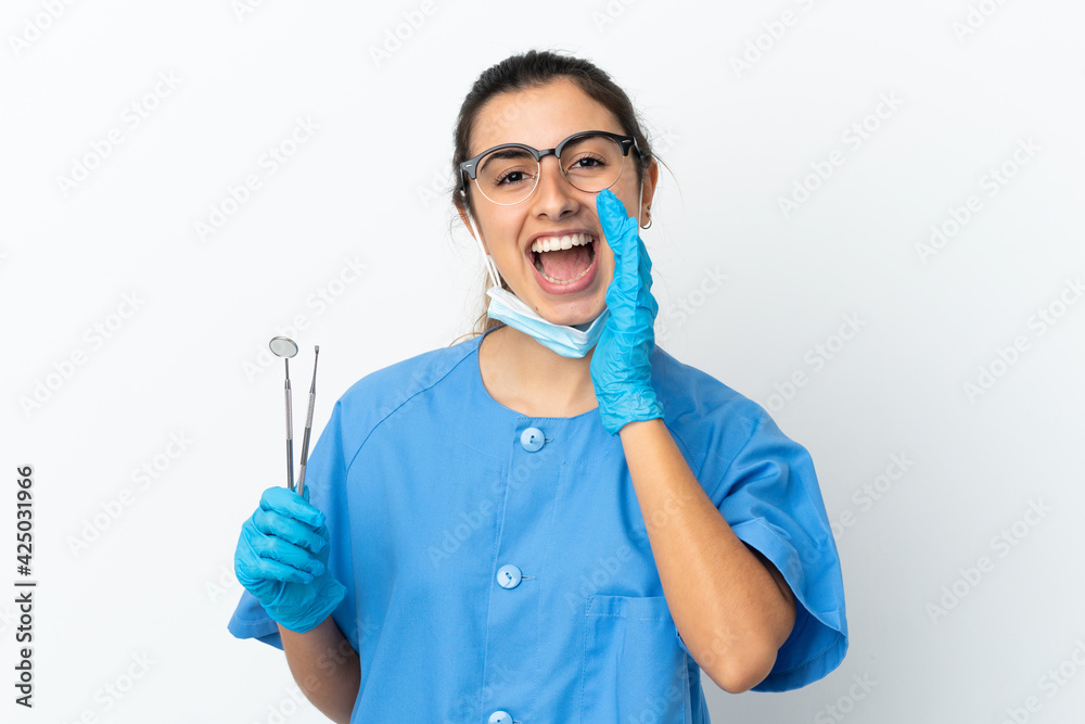 Young woman dentist holding tools isolated on white background shouting with mouth wide open Young woman dentist holding tools isolated on white background shouting with mouth wide open