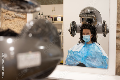 Young brunette lady looks to camera while hairdryer works