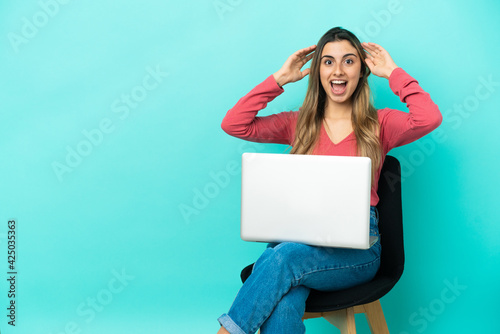 Young caucasian woman sitting on a chair with her pc isolated on blue background with surprise expression © luismolinero