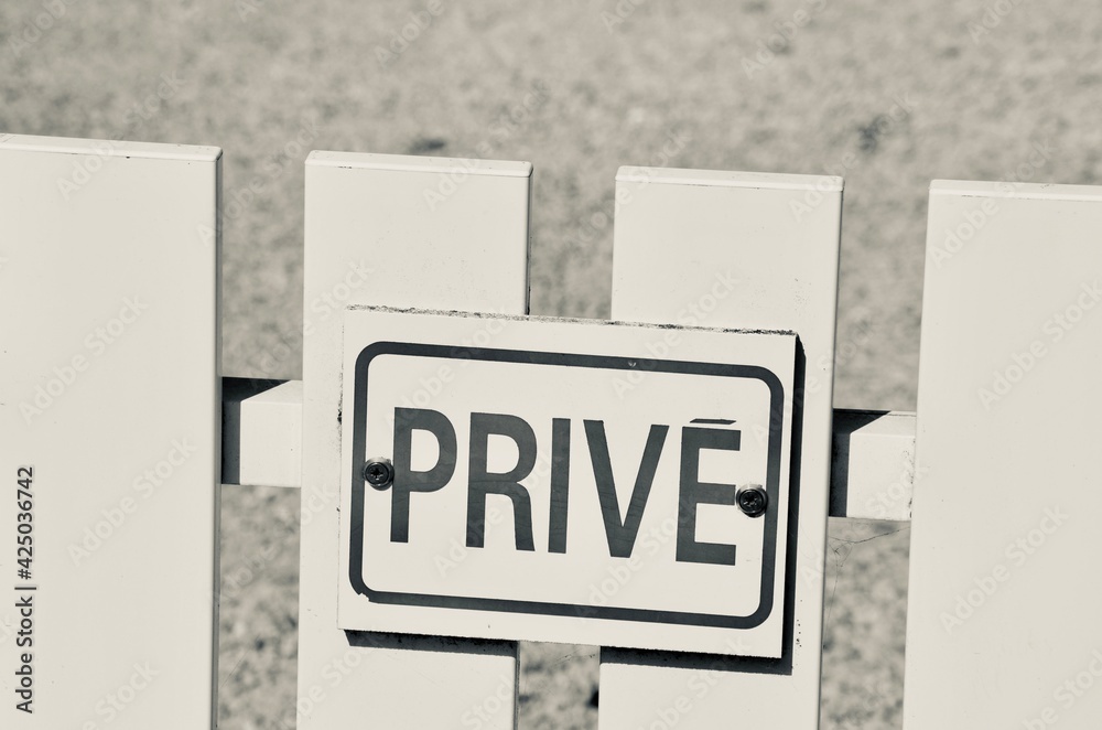 Wooden white fence closeup, a shield with the word privé (french for private) on it, creative black and white vintage style, blurred gravel path background, a sunny day