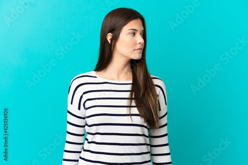 Teenager Brazilian girl over isolated blue background looking to the side