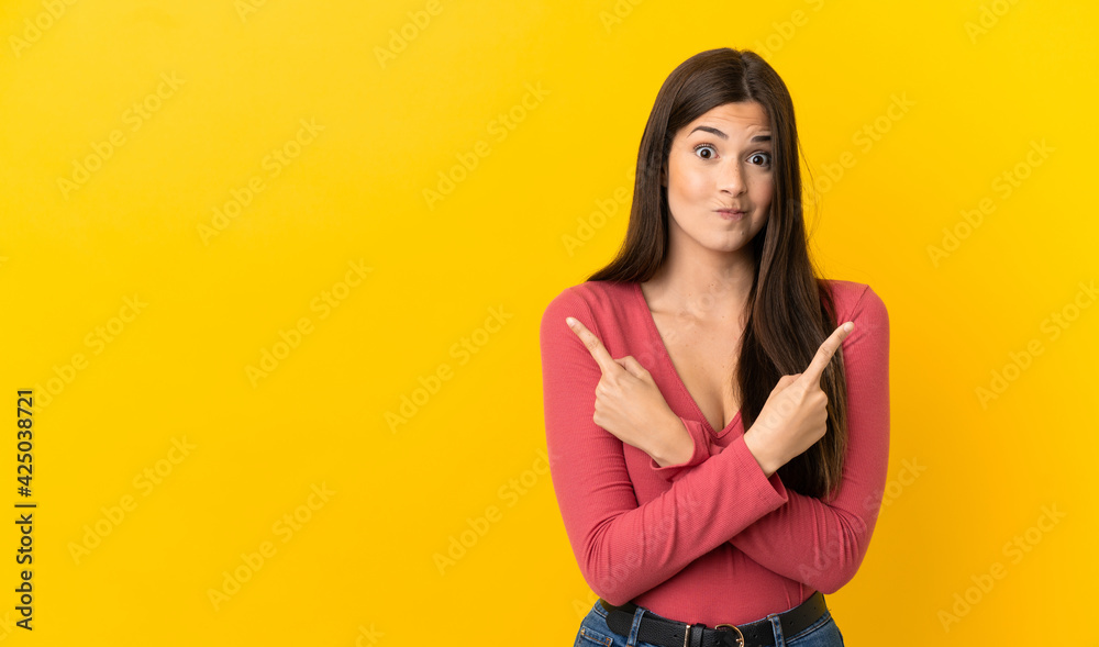 Teenager Brazilian girl over isolated yellow background pointing to the laterals having doubts