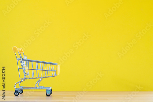 Shopping cart toy from the supermarket on table with yellow background, Sale buy mall market shop consumer concept. Copy space