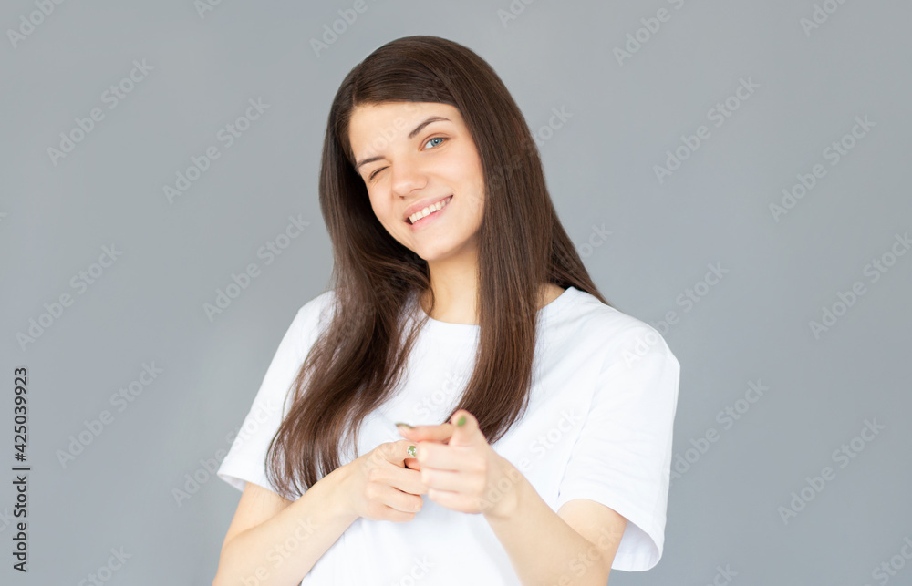 Smiling happy woman pointing at the camera with both hands and her head tilted to the side with a playful expression and focus to her face over grey Smiling happy woman pointing at the camera with both hands and her head tilted to the side with a playful expression and focus to her face over grey