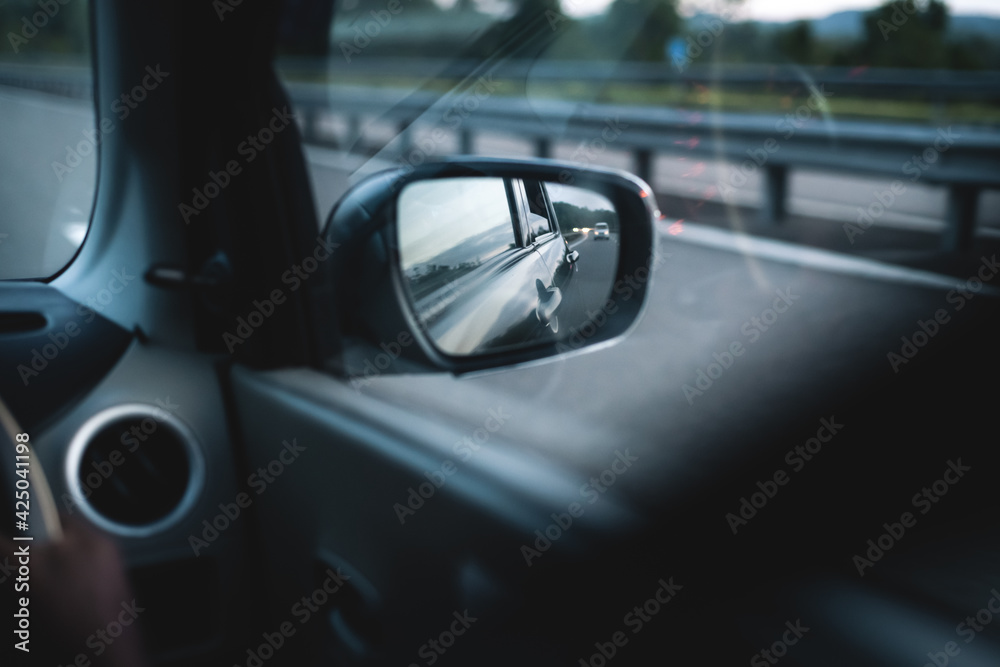 Car side mirror and the reflecting evening sunlight from the car body and glowing in the highway. fast-moving automobile concept. side mirror view from the rear passenger sheet.