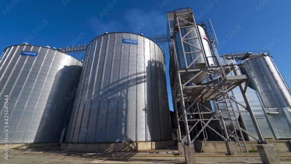 Modern factory for storage crop. Metal grain elevators on agricultural complex. Exterior of industrial plant under blue sky. Modern factory for storage crop. Metal grain elevators on agricultural complex. Exterior of industrial plant under blue sky.