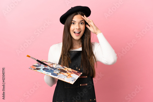 Young artist girl holding a palette over isolated pink background with surprise expression
