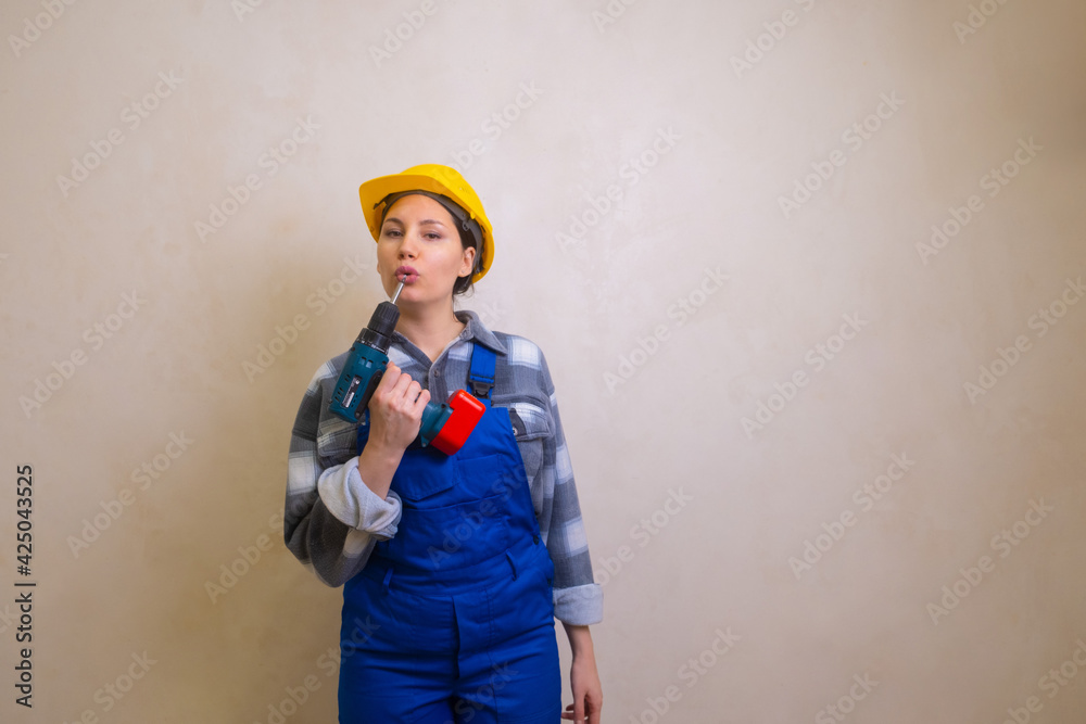 A girl in a blue construction worker's overalls and a yellow hard hat holds a screwdriver in her hands and pretends to blow on the barrel of a gun