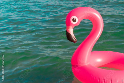 Beach flamingo. Pink inflatable flamingo in blue sea water on summer ocean beach background. Trendy summer concept. © Maksym