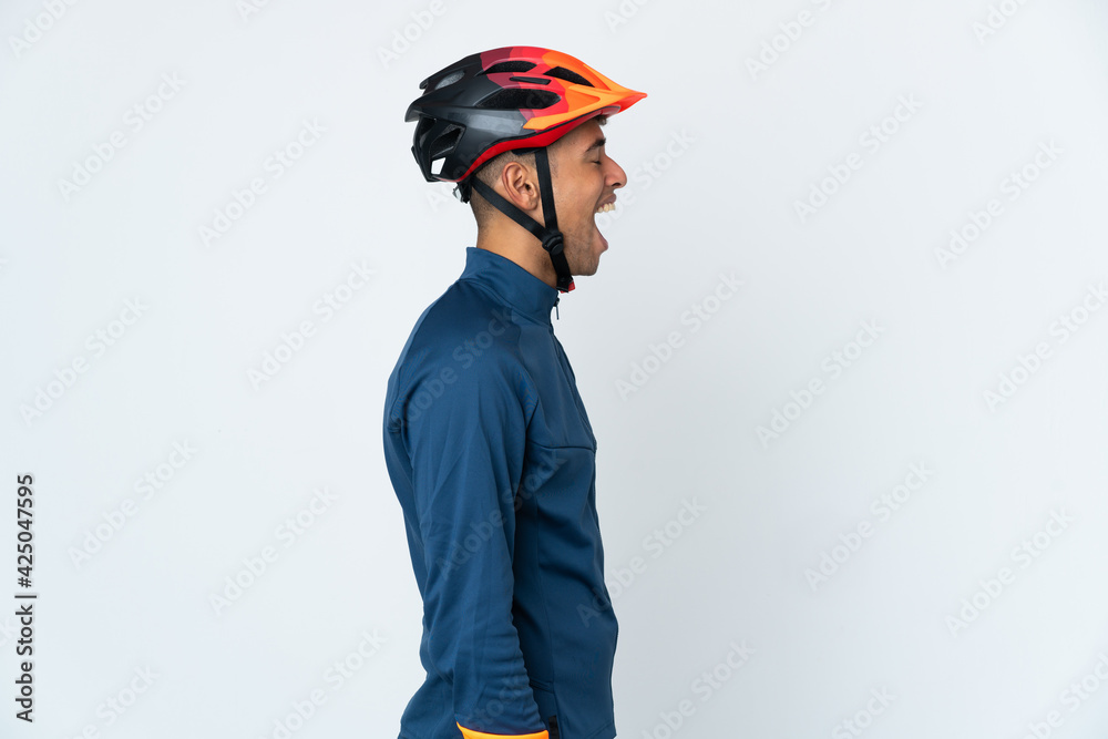 Young cyclist Brazilian man isolated on white background laughing in lateral position - obrazy, fototapety, plakaty 