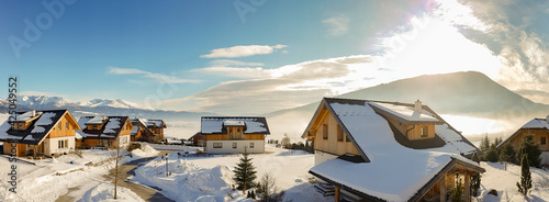 Snowy housing estate in the mountains with houses. In the background the Alps and a cloudy sky. Copy space