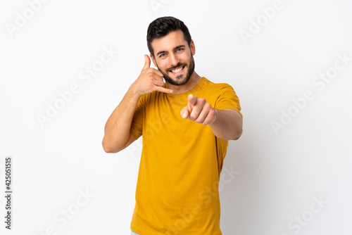 Young handsome man with beard isolated on white background making phone gesture and pointing front