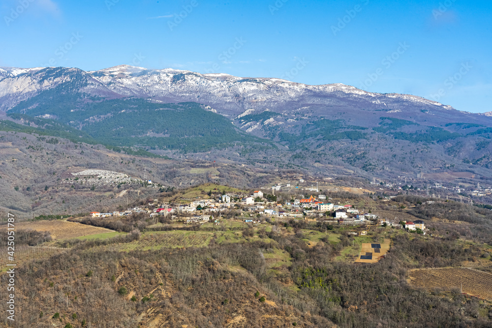 Panoramic view of the snow-capped mountains and the mountain village at their foot in early spring