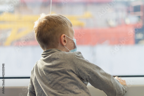 A Caucasian boy in a medical protective mask travels on a train and looks out the window