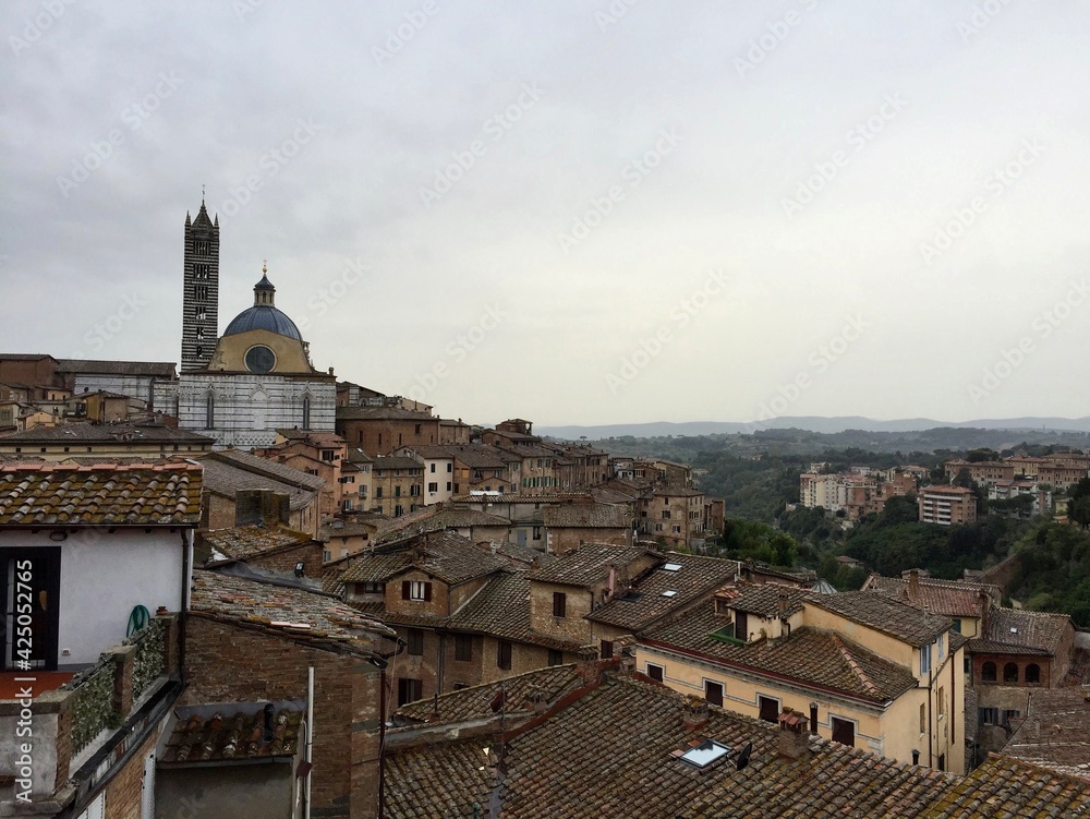 Panorama view of Siena medieval buildings. Evening, cloudy sky, Tuscany hills on a background, tile rooftop. Italy 