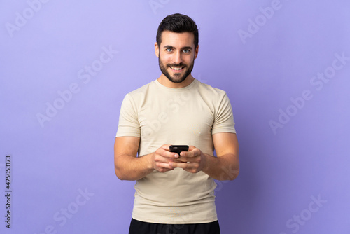 Young handsome man with beard over isolated background sending a message with the mobile