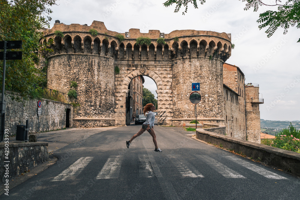 Narni, Umbria, Italy - The medieval cathedral of San Giovenaleo in the ancient village of Narni. Entrance to the city. Main gate. A girl crosses the road at a pedestrian crossing