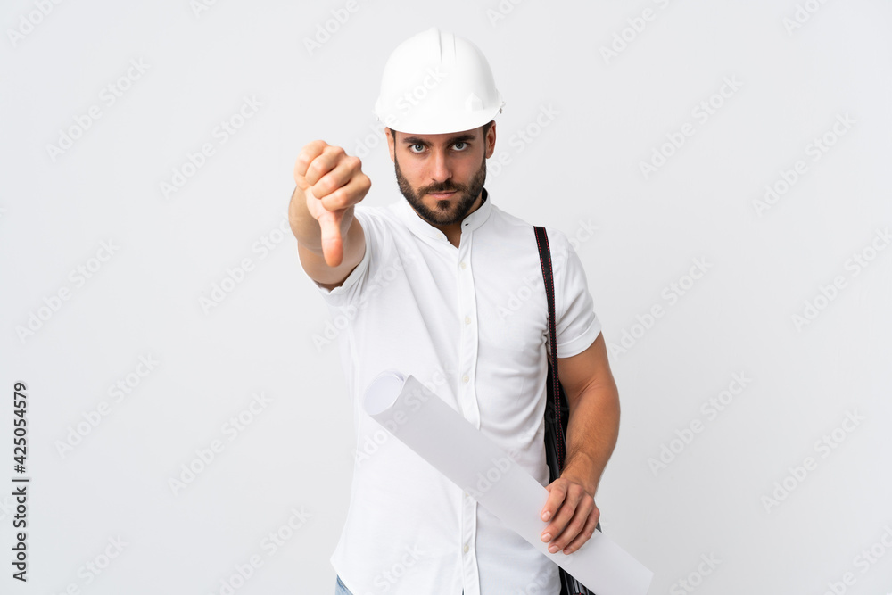 Young architect man with helmet and holding blueprints isolated on white background showing thumb down with negative expression Young architect man with helmet and holding blueprints isolated on white background showing thumb down with negative expression