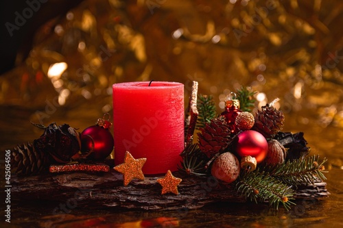 Wreath with a red candle, gold stars, ornaments on a tree bark, golden background