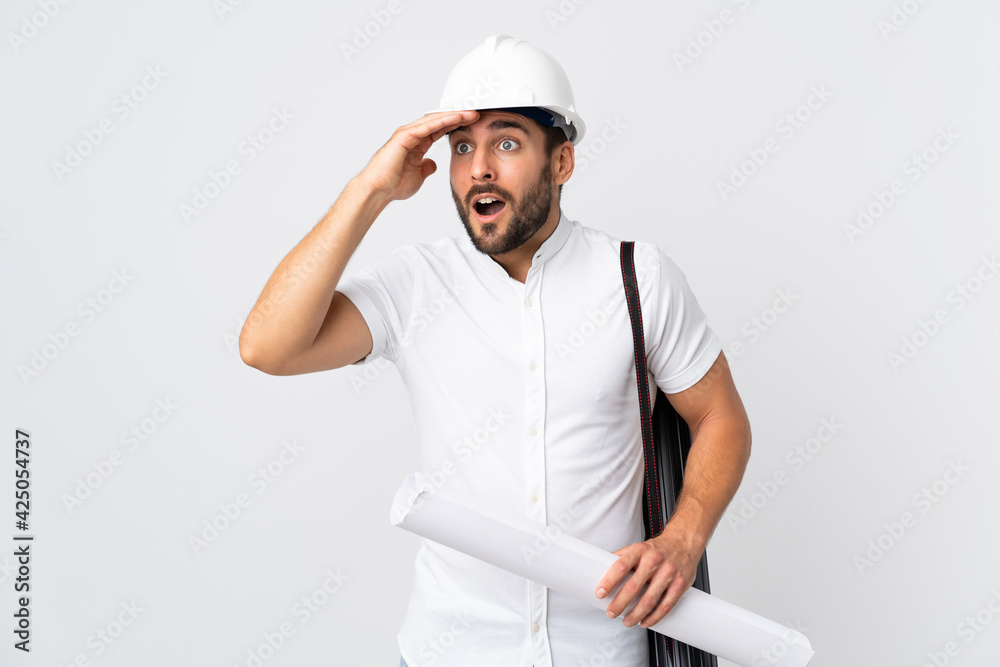Young architect man with helmet and holding blueprints isolated on white background with surprise expression while looking side Young architect man with helmet and holding blueprints isolated on white background with surprise expression while looking side